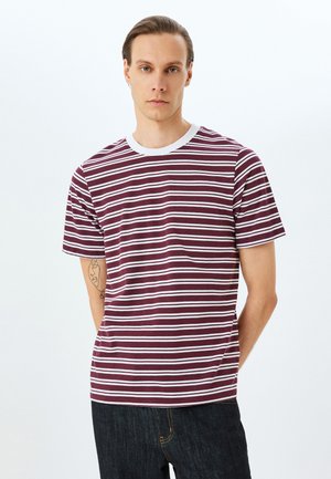 Camiseta de rayas burdeos y blancas con cuello redondo, mangas cortas y textura suave de algodón, combinada con jeans oscuros.