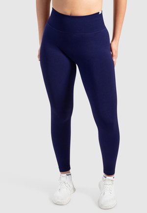 Marineblauwe leggings van rekbaar materiaal, met een hoge tailleband, een gladde textuur en een figuurvormend ontwerp, gecombineerd met witte sportschoenen.