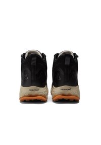 Un paio di scarpe da trail running nere con suole intermedie beige texture e suole arancioni, viste da dietro su uno sfondo bianco.