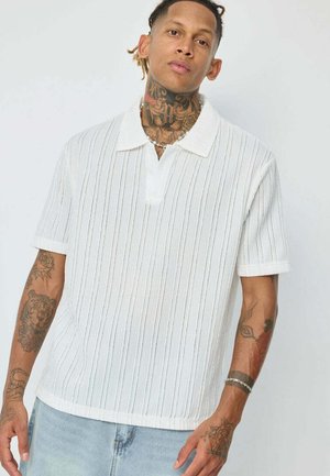 Polo shirt blanc à manches courtes avec des rayures verticales, un col à encoches, un tissu texturé et une coupe décontractée, associé à un denim bleu clair.