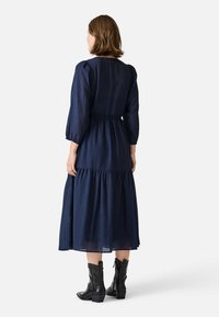 Navyblaues Langarmkleid mit strukturiertem Stoff, elastischem Bund und schichtweisem Rock. Kombiniert mit schwarzen Stiefeletten.