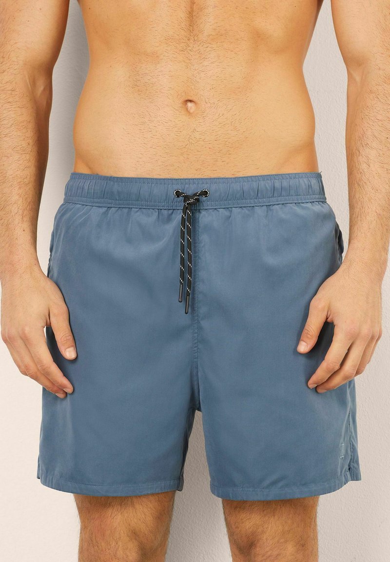 Pánské plavky v jemné modré tkanině; elastický pas s černou šňůrkou; boční kapsy; střih až po kolena; jednobarevné, bez vzorů.
