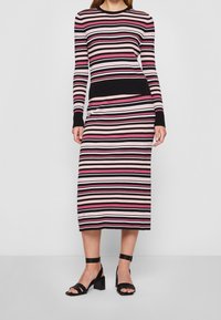 Robe tricotée à manches longues ; présente des rayures alternées en rose, noir et blanc. Motif texturé en côtes ; sandales noires à bride de cheville.