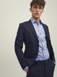 Completo blu navy con un motivo a scacchi, design a un petto. Camicia leggera blu con motivo sotto, dotata di dettagli con bottoni e colletto.
