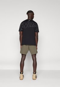 Black cotton t-shirt with large graphic lettering in gray on the back, worn with olive shorts and beige ankle boots. Simple design and fit.