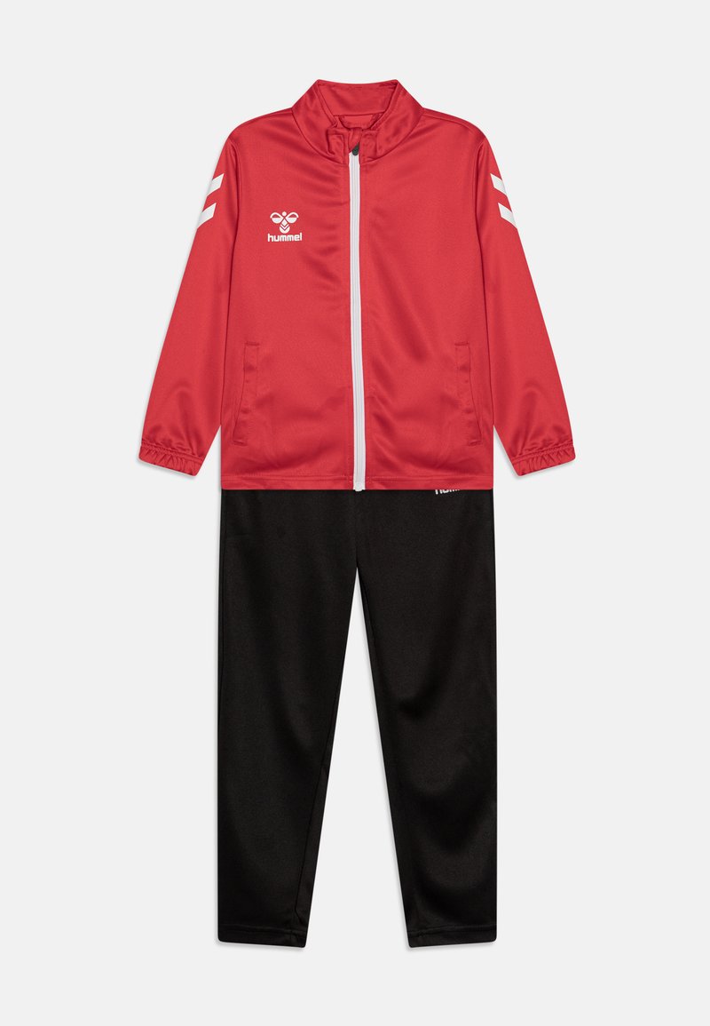 Sarkans ar rāvējslēdzēju augšpusē un augstu apkakli, ar baltām akcentiem; kopā ar melnām biksēm. Izgatavots no gludas, vieglas auduma. Satur logo uz krūtīm.