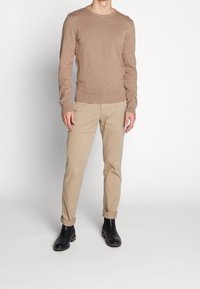 Maglione marrone chiaro in un morbido tessuto a maglia, abbinato a chinos beige arrotolati e stivali neri in pelle alla caviglia. Design semplice e aderente con scollatura rotonda.