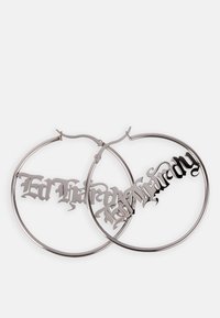 Pendientes de aro de plata con letras recortadas y en un estilo de fuente dramático. El diseño presenta un acabado pulido y un detallado intrincado.