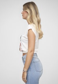 Kuttet hvit t-skjorte med oppbrettede ermer og grafisk trykk; høytlivs lyseblå denimjeans med baklommer; minimale tilbehør.