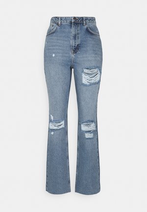 Pantalones vaqueros de mezclilla azul con cintura alta, piernas acampanadas, detalles desgastados y parches rasgados en la parte delantera. Tejido texturizado con costuras visibles.