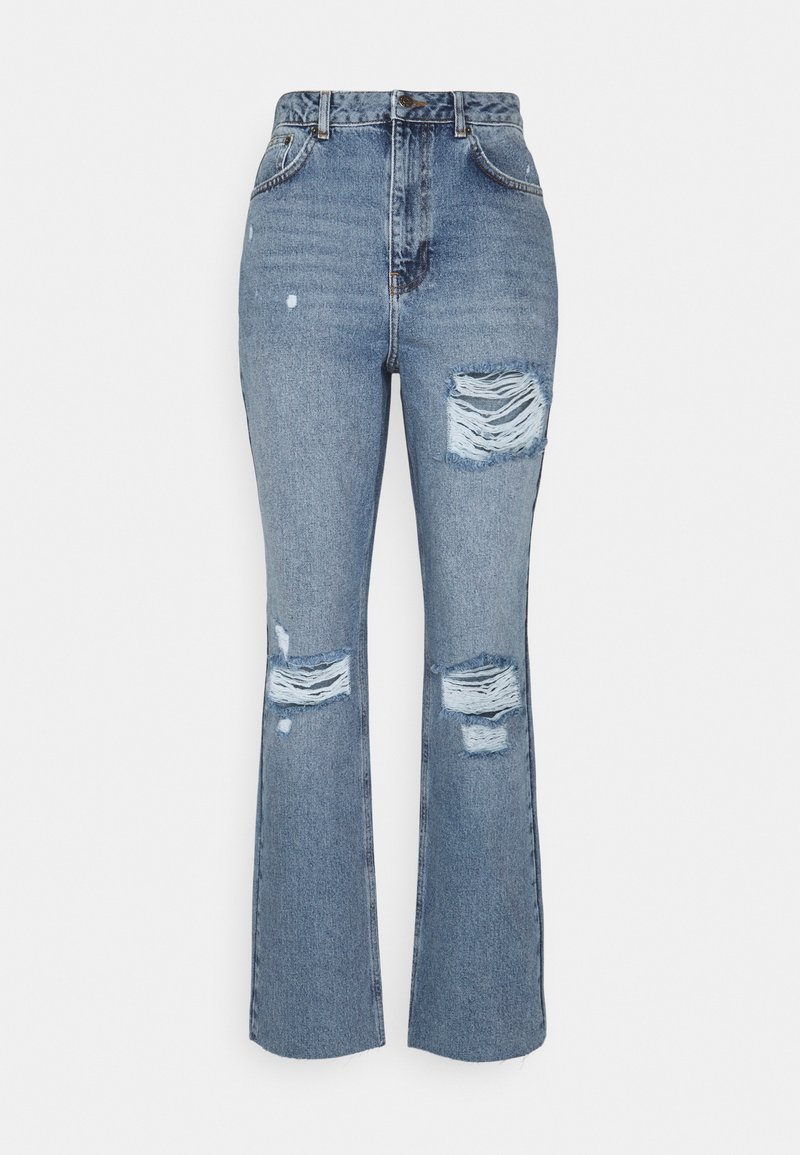 Pantalones vaqueros de mezclilla azul con cintura alta, piernas acampanadas, detalles desgastados y parches rasgados en la parte delantera. Tejido texturizado con costuras visibles.