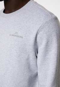 Grå crewneck sweatshirt i mjukt tyg. Har en subtil grön "J.LINDEBERG"-logotyp broderad på vänster bröst.