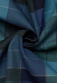 Tessuto tartan blu e verde attorcigliato al centro, che mostra un dettagliato intreccio diagonale e fini linee di cucitura gialle e bianche.