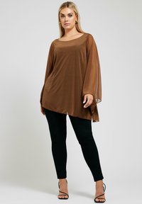 Top marrone, trasparente, a maniche lunghe con una vestibilità ampia, caratterizzato da un delicato motivo a pois. Abbinato a pantaloni neri aderenti e tacchi neri con cinturini.