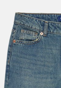 Heledad teksased, millel on helesinine värv, klassikaline viie tasku disain ja vaskse riistvara aktsendid. Tekstuur on pehme ja kerge kulumisjälgede märkidega.