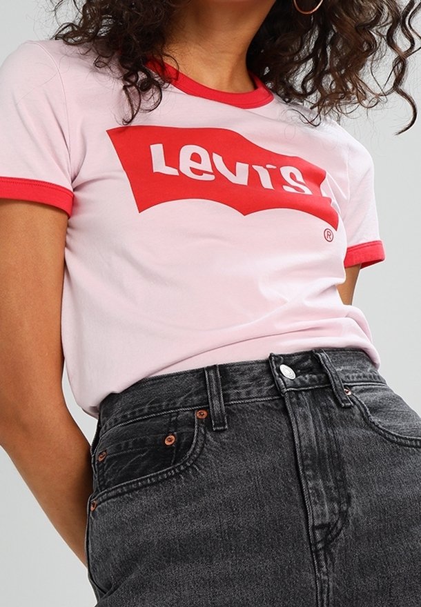 Ljust rosa t-shirt med röd ringkrage som har en vit "Levi's" logotyp. Matchad med höga svarta jeans som visar metalliska detaljer.