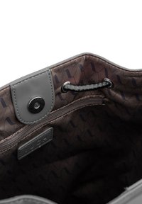 Šedý interiér tašky se zaklapávacím uzávěrem, obsahující jemný vlnitý vzor v tmavě hnědé barvě. Obsahuje zipovou kapsu a značkovou štítek.