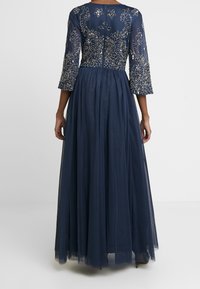Vestido de noche azul marino con mangas tres cuartos, cuerpo adornado con intrincados abalorios y una falda de tul fluida.
