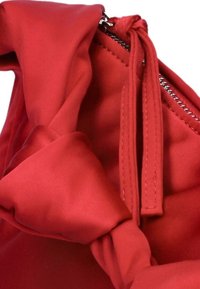 Rood stoffen handtas met een gestrikt knoopdetail, een soepele textuur en een zilveren ritssluiting langs de rand. Het ontwerp is zacht en gestructureerd.