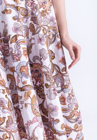 Robe blanche ornée d'un motif cachemire coloré en rose, violet et or. Tissu léger à la texture douce et ourlet évasé.