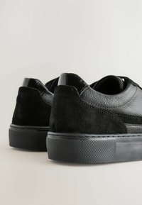 Schwarze Sneaker mit einem strukturierten Lederoberteil und einer Wildleder-Ferse, ausgestattet mit einer Gummisohle und minimalistischen Designelementen.