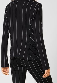 Haut noir à manches longues avec des rayures verticales blanches, doté d'une coupe décontractée et d'une texture lisse, associé à un pantalon à rayures assorti.