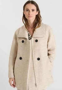 Beige jas van een wolmix met een comfortabele pasvorm, een grote kraag, twee zwarte knopen en zijzakken; heeft een trekkoordsluiting aan de voorkant.