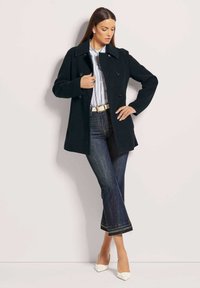 Black wool coat with a thick collar and double-breasted buttons, paired with denim flared jeans and white pointed-toe shoes.