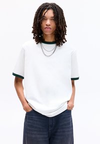 Hvid t-shirt med grønt ribbet krave og manchetter, let oversized pasform, parret med mørk denim shorts. Har en sølv kædehalskæde.