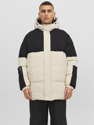 Daunenjacke mit einem beigefarbenen Oberteil, schwarzen Akzenten und Kapuze. Das Material ist glatt mit einer gesteppte Textur. Inklusive elastischer Bündchen und Nähte.