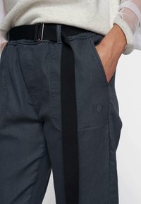 Pantaloni grigio scuro con una striscia laterale nera, realizzati in tessuto testurizzato, con vita elasticizzata e tasche laterali. Dettaglio ricamato con il numero 10.