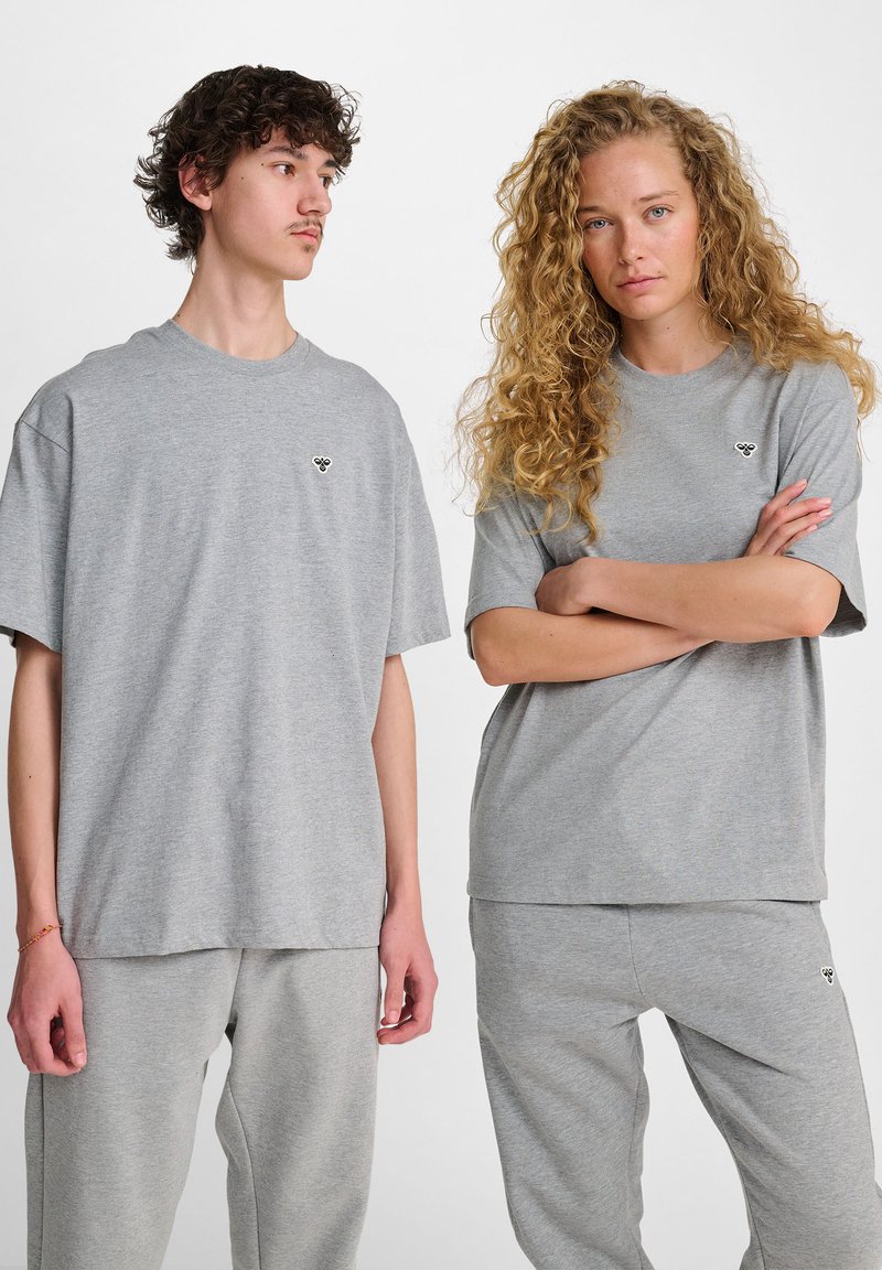 Camisetas de algodón grises con mangas cortas, que presentan un pequeño logo en el lado izquierdo del pecho. Combinadas con pantalones de chándal grises a juego. Textura suave.