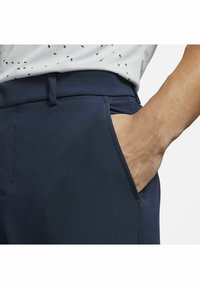 Marinblå byxor med en mjuk struktur, med en sidficka och en smal passform. Synlig detalj på midjebandet.