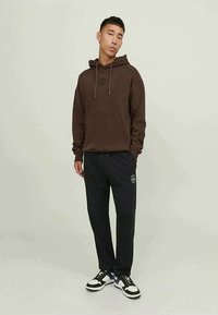 Brown hooded sweatshirt with drawstrings, kangaroo pocket; paired with black joggers featuring a logo, worn with black and white sneakers.