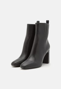 Schwarze Leder-Ankle-Boots mit glatter Oberfläche, spitzem Zehenbereich und Blockabsatz. Mit Schlaufen an der Rückseite für ein einfaches An- und Ausziehen.