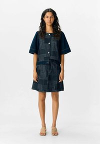 Ensemble en denim composé d'une veste à manches courtes avec de grands boutons et d'une jupe à motifs. Les deux sont d'un bleu foncé avec un design texturé.