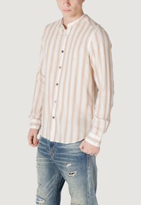 Camicia a righe beige chiaro con righe verticali arancio e bianche, maniche lunghe, colletto con bottoni e bottoni a contrasto, abbinata a jeans blu strappati.