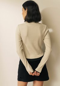 Haut à manches longues beige côtelé avec une silhouette ajustée et un ourlet court, associé à une mini-jupe en cuir suédé noire.