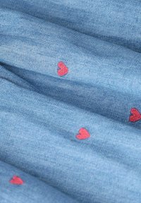 Tissu en denim de couleur bleu clair avec de petits cœurs rouges brodés éparpillés sur la surface. Texture douce, design léger.