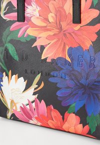Svart veske med livlig blomstertrykk i rosa, oransje, blått og hvitt. Har hevet "TED BAKER LONDON"-logo og teksturert overflate.