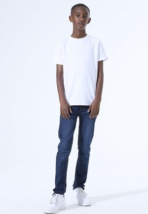 Witte t-shirt met korte mouwen, blauwe denim jeans en witte sneakers. Eenvoudig ontwerp met een losse pasvorm, zachte stof en neutrale kleuren.
