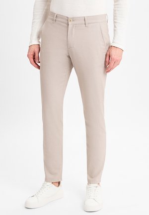 Beige Slim-Fit-Hosen aus leichtem Stoff, mit einem Knopfverschluss, zwei vorderen Taschen und kombiniert mit weißen Sneakers.
