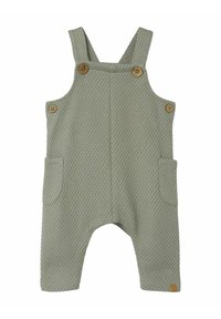 Pantalones de tirantes de algodón tejido en verde claro, con tela texturizada, botones de madera, dos bolsillos laterales y un pequeño parche con el logo en el dobladillo.