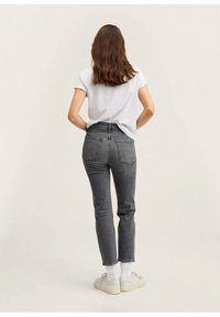 Jeans grigi alti in vita con gamba dritta, dotati di tasche posteriori e una finitura sbiadita. Abbinati a una maglietta bianca e scarpe da ginnastica.