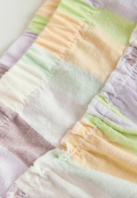 Gros plan sur un tissu à carreaux doux de couleur pastel, avec des bords froncés élastiqués et des détails de couture visibles.
