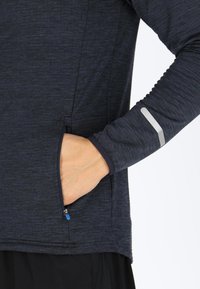 Navy long-sleeve athletic top with a zippered side pocket, textured fabric, and reflective accent on the sleeve, designed for active wear.