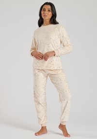 Set di abbigliamento loungewear beige con puntini dorati sparsi, composto da una maglietta a maniche lunghe con collo rotondo e pantaloni con polsini elasticizzati. Tessuto morbido.