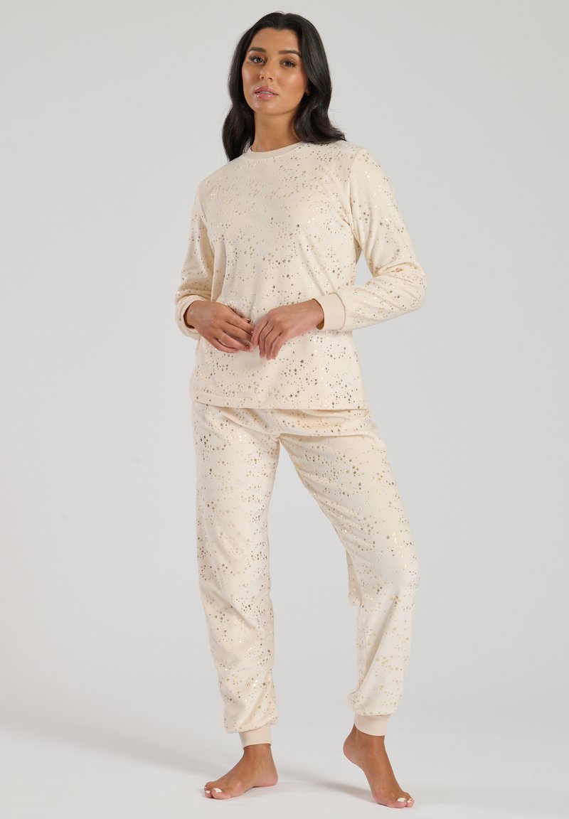 Set di abbigliamento loungewear beige con puntini dorati sparsi, composto da una maglietta a maniche lunghe con collo rotondo e pantaloni con polsini elasticizzati. Tessuto morbido.