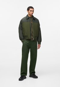 Chaqueta bomber verde oliva con cierre delantero y puños acanalados, combinada con pantalones verdes a juego y zapatillas negras, creando un look monocromático.