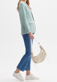 Mint green blazer, light blue flared jeans, and white sneakers. Model holds a beige, drawstring shoulder bag. Simple design and clean colors.